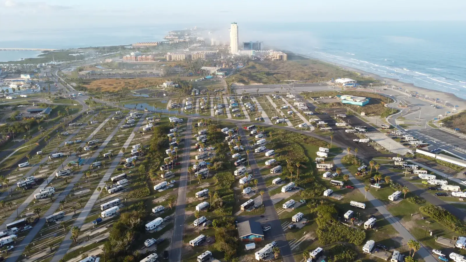 Aerial view of a large RV park with numerous white recreational vehicles parked in organized rows among palm trees, with
