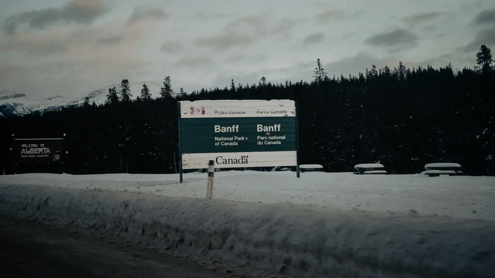 Banff National Park entrance sign in snow with coniferous forest and snow-capped mountains in background