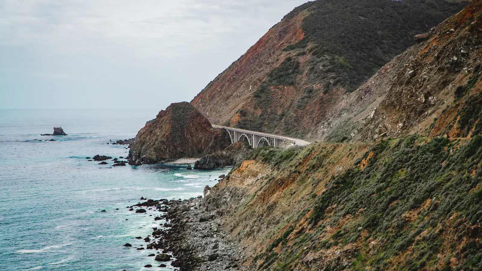 Arched bridge spanning rocky coastal cliffs above turquoise ocean waters