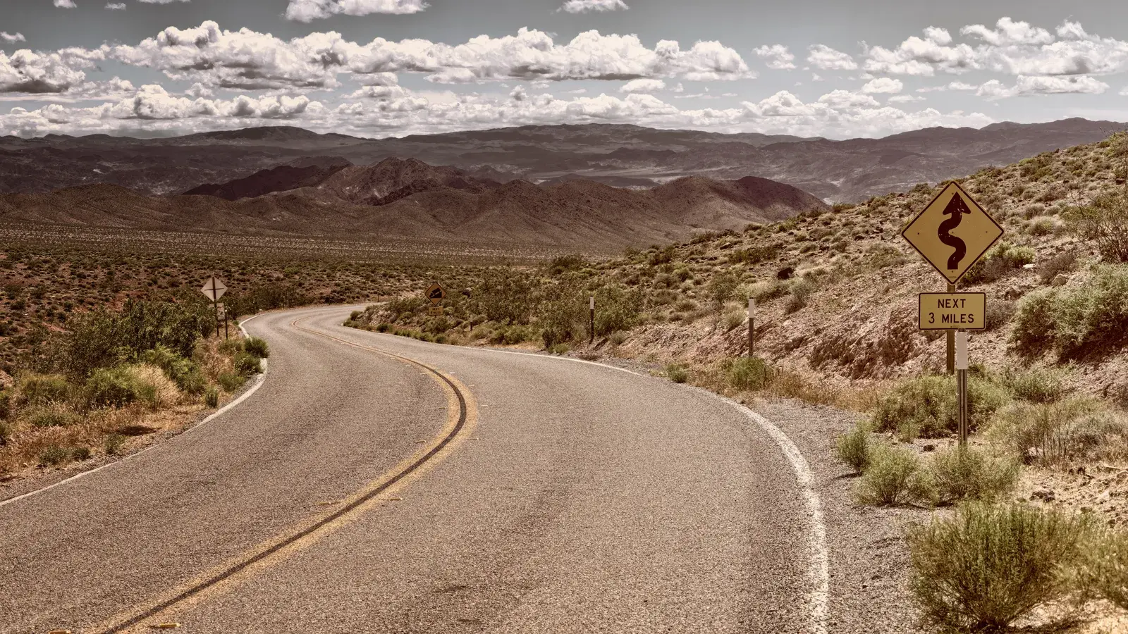Curved desert road in arid landscape with mountains and clear sky