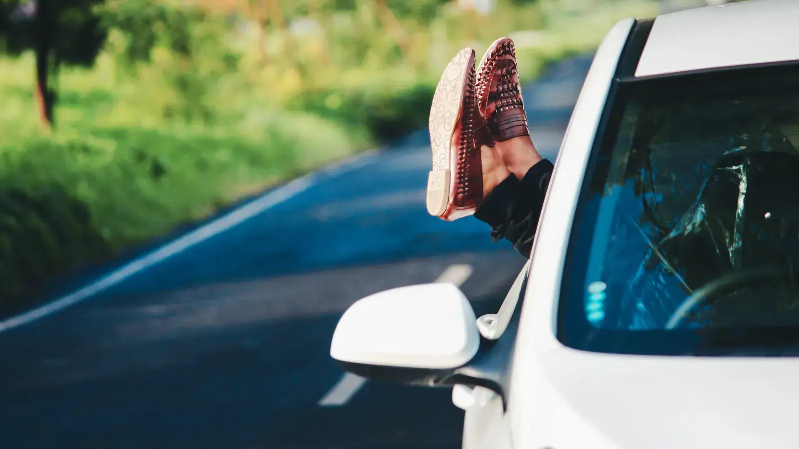Person with feet resting out of a car window on a scenic road with green countryside in the background