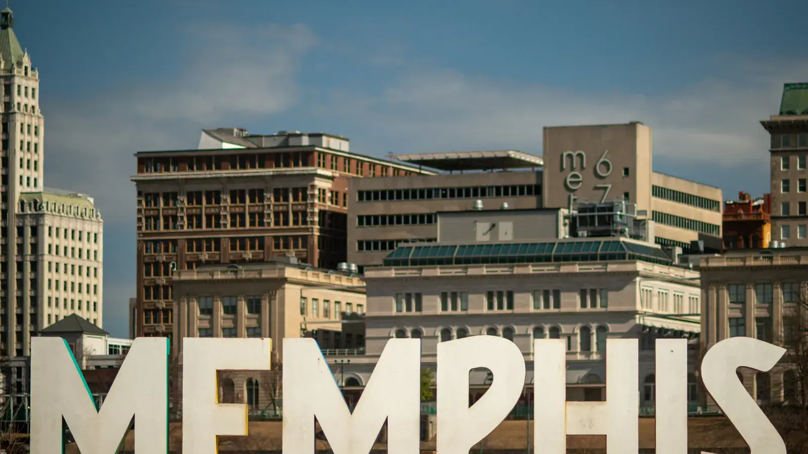 Large white Memphis sign in foreground with historic downtown buildings and skyline behind it under blue sky