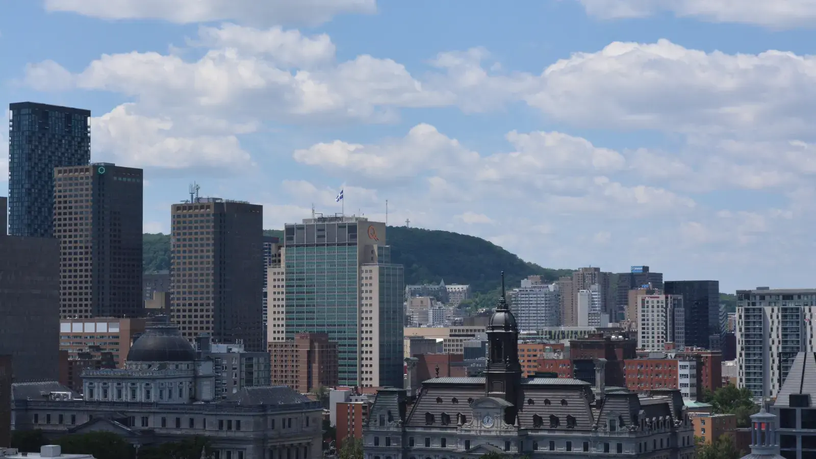 Montreal skyline with downtown skyscrapers, historic buildings with domes in the foreground, and a forested hill in the