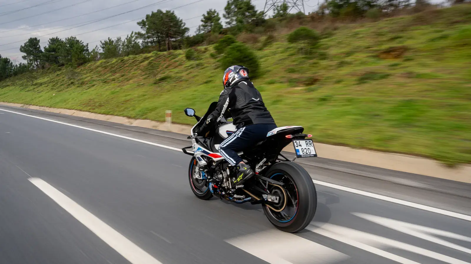 Motorcyclist in black jacket and red helmet riding on a highway with green hillside in background