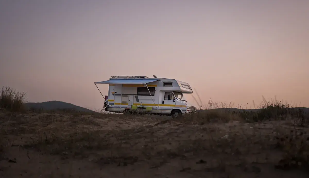 Motorhome with blue awning parked in desert landscape at dusk