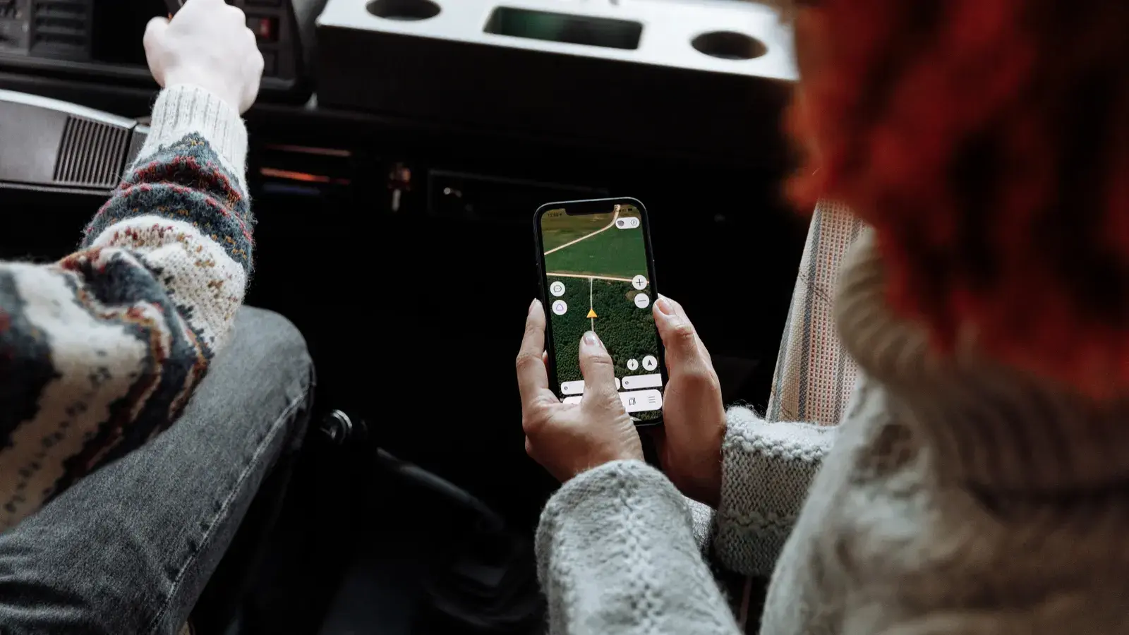 Person holding a smartphone displaying a navigation app with a road map and directional controls inside a car