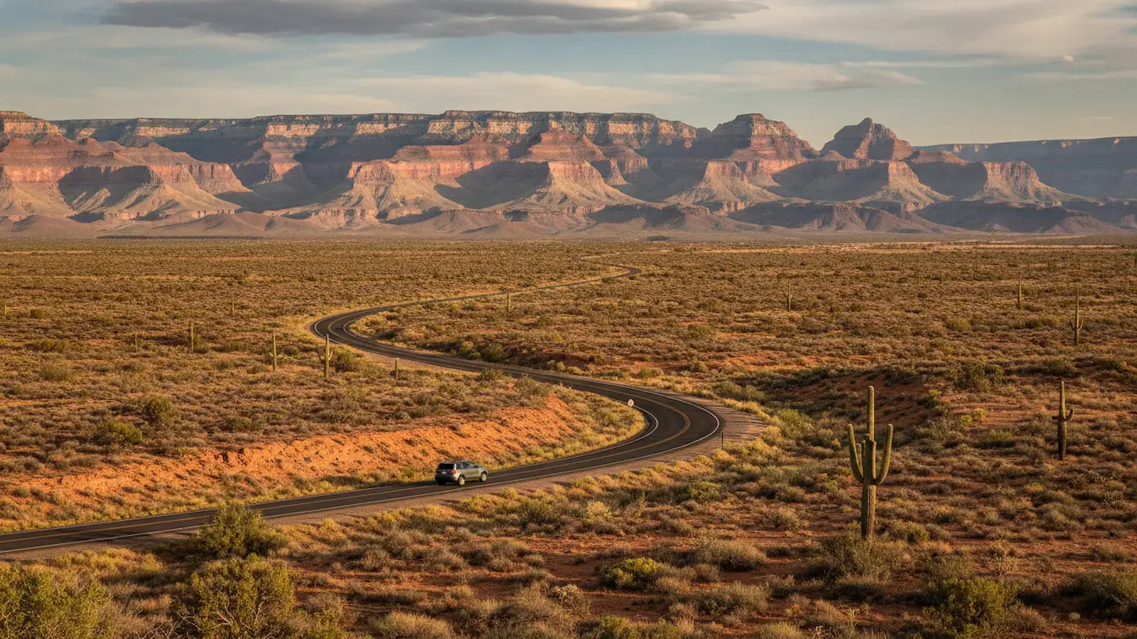 Winding desert highway with a car driving through arid landscape dotted with saguaro cacti, with layered mesa formations