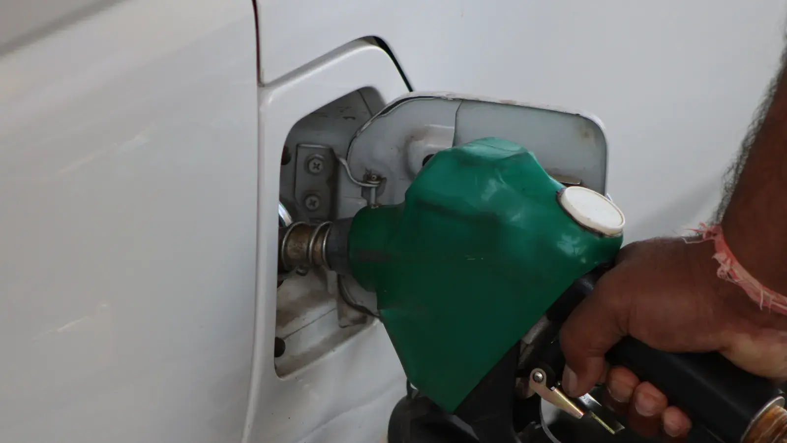 Hand holding a green fuel nozzle inserted into a white car's gas tank opening