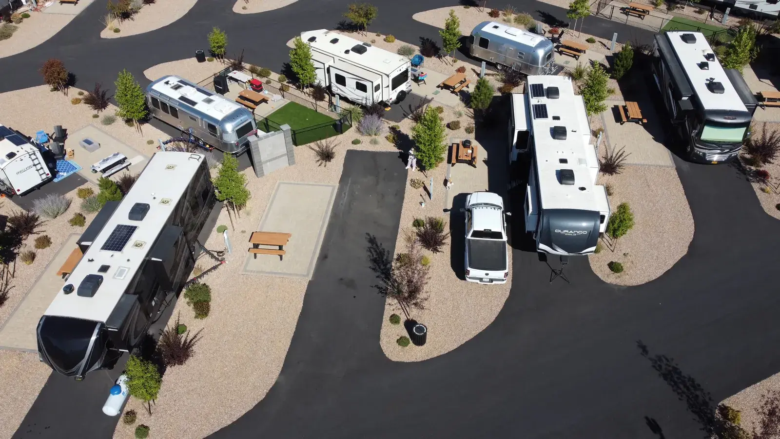 Aerial view of an RV park with multiple trailers and motorhomes parked in individual sites with landscaping and paved roads