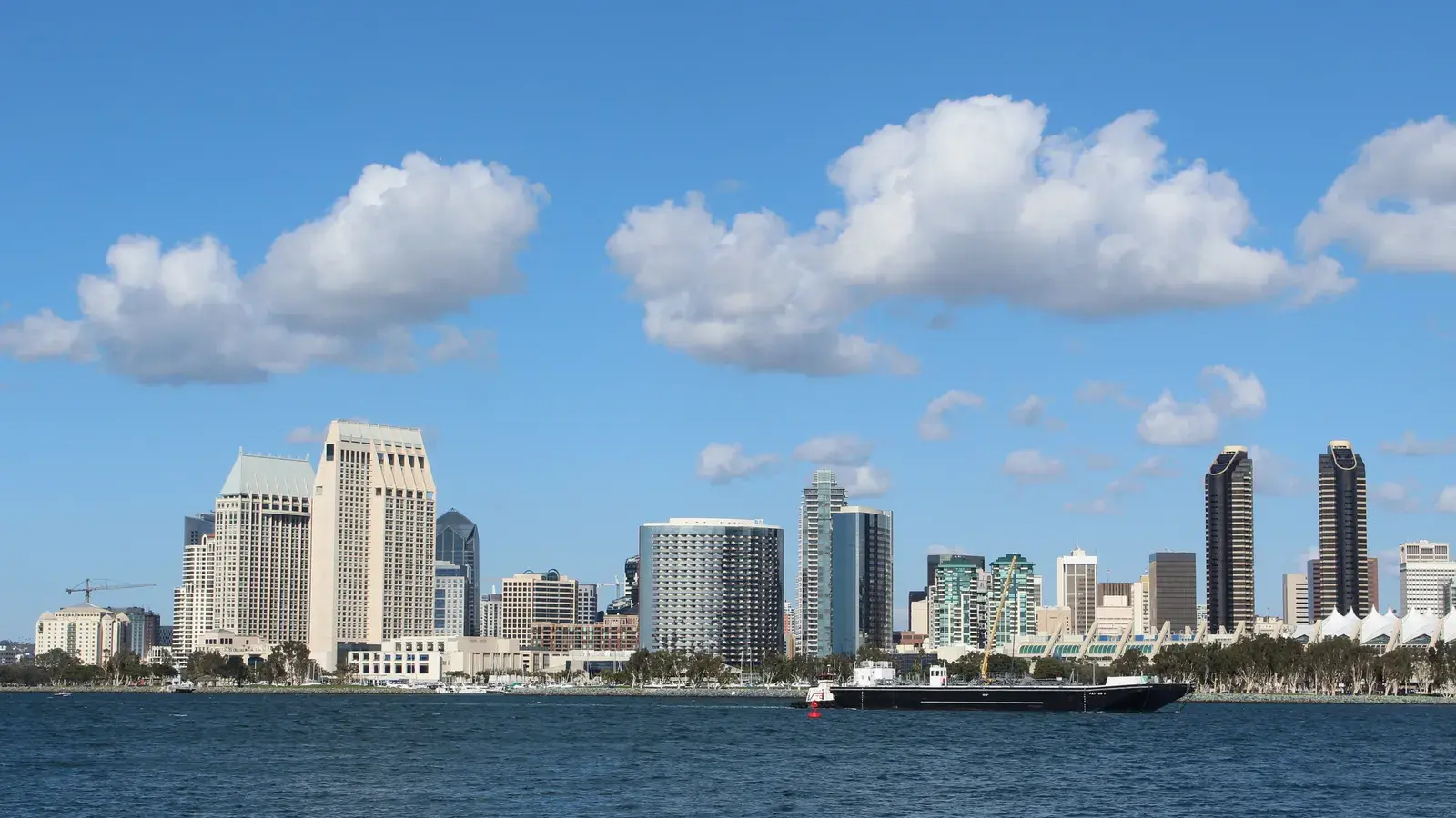 San Diego skyline with high-rise buildings along the waterfront under a blue sky with white clouds