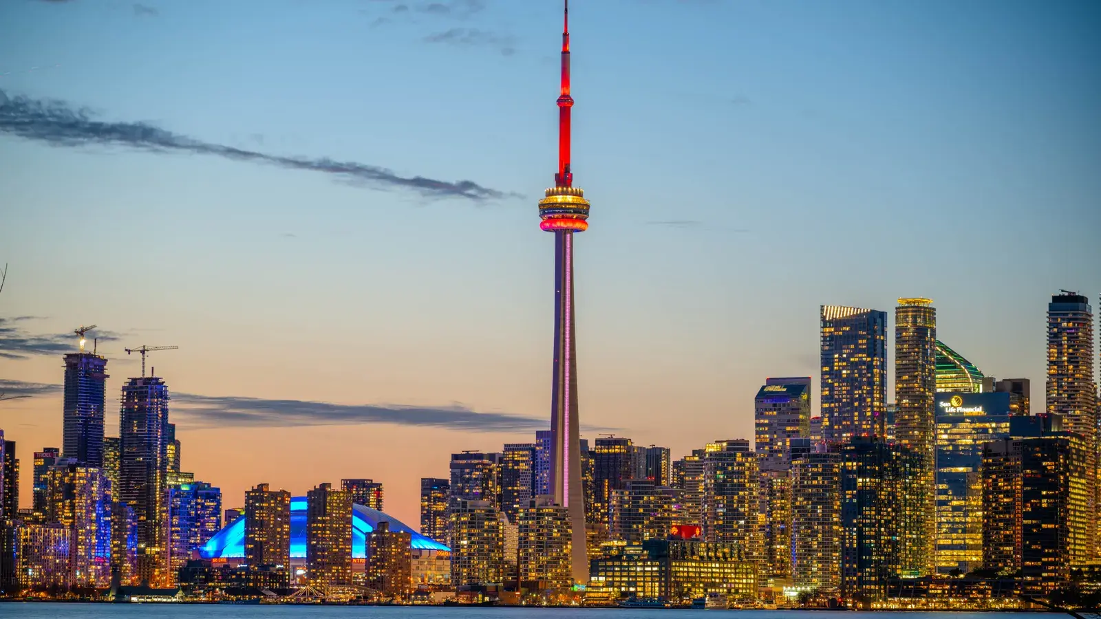 Toronto skyline at dusk with illuminated CN Tower and lit skyscrapers reflected in the water below