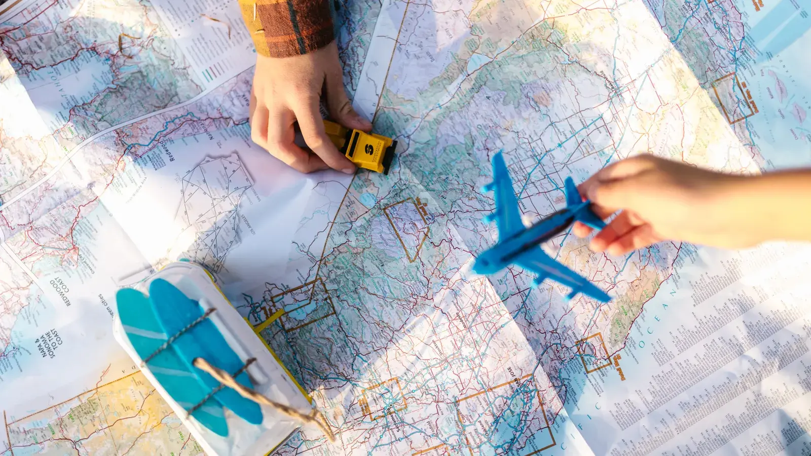 Hands holding toy airplane and car over colorful road maps in sunlight