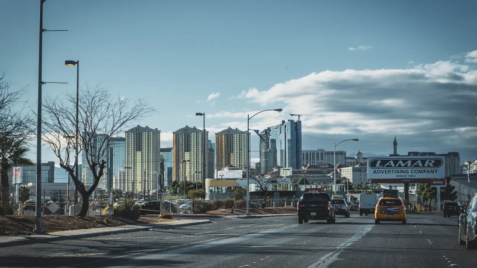 Urban street with traffic and tall buildings in the distance under a blue sky with clouds