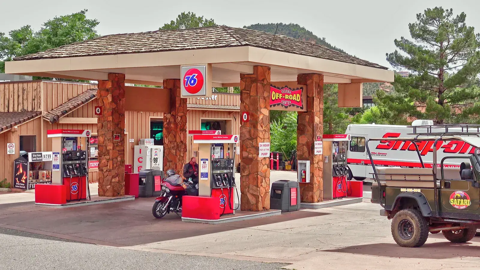 Vintage-style gas station with red and cream exterior, large stone pillars, and a motorcycle parked at the pumps